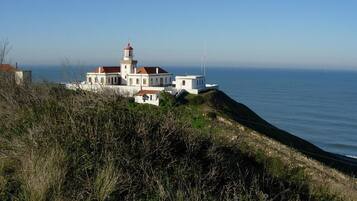 A coastal building with a lighthouse, situated on a grassy hill overlooking the sea.