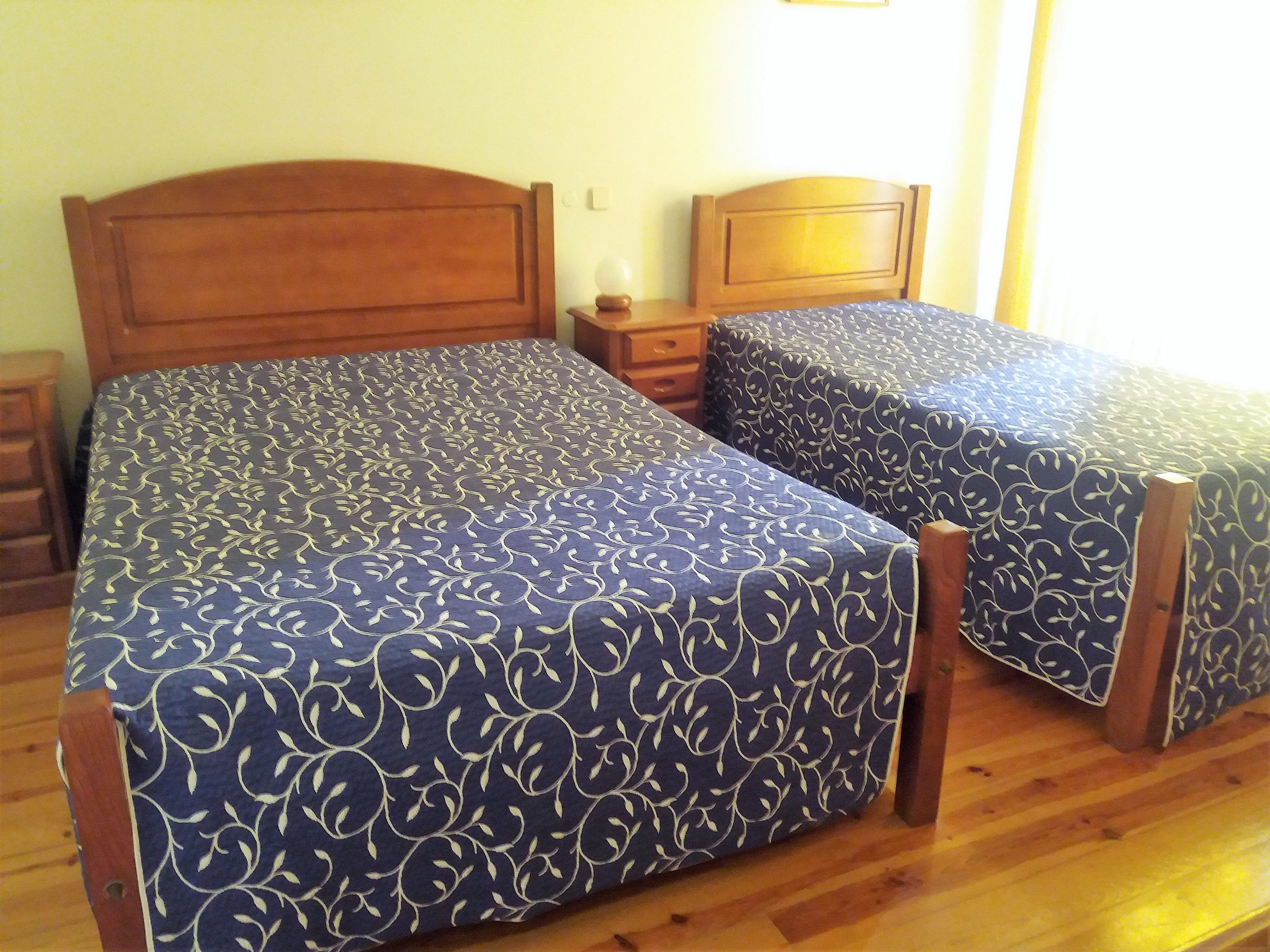 A double bed with a floral-patterned bedspread, a wooden headboard, and a nightstand with a lamp.