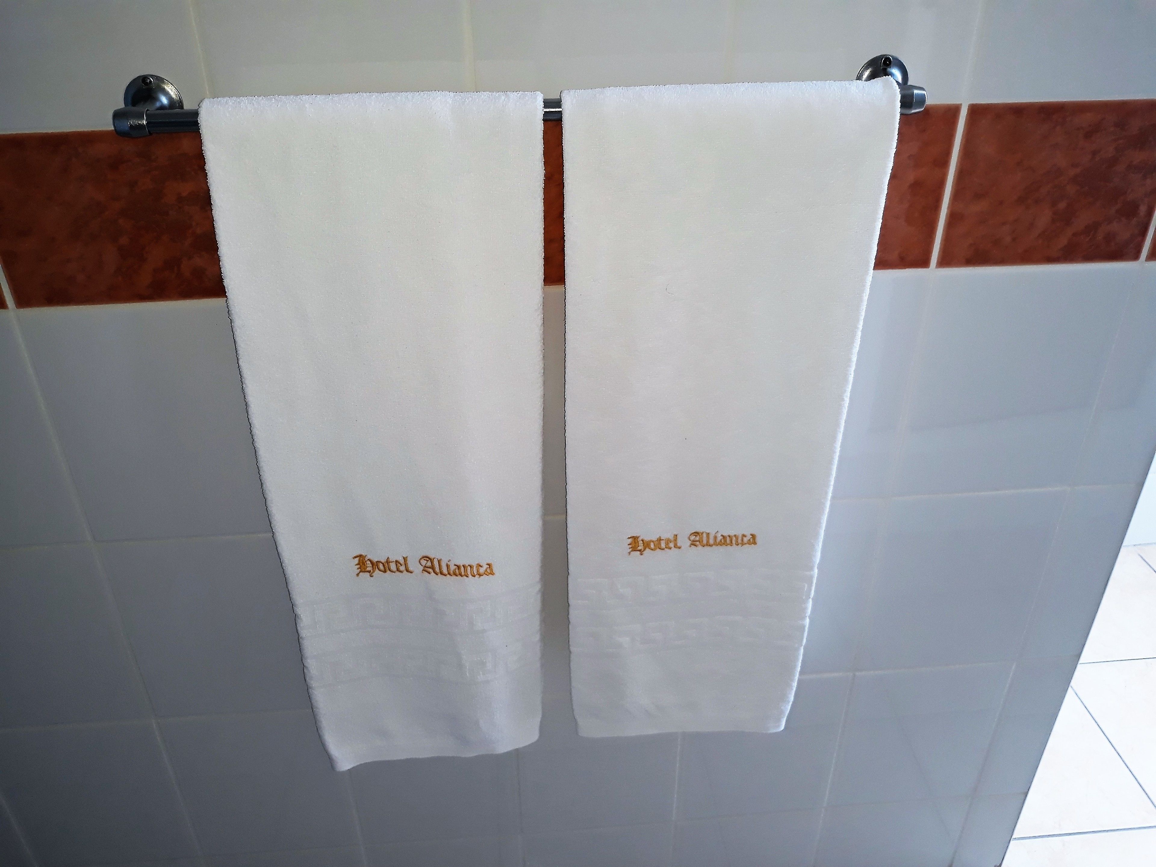Two white towels hanging on a metal towel rack with the text "Hotel Alianza" embroidered on them.