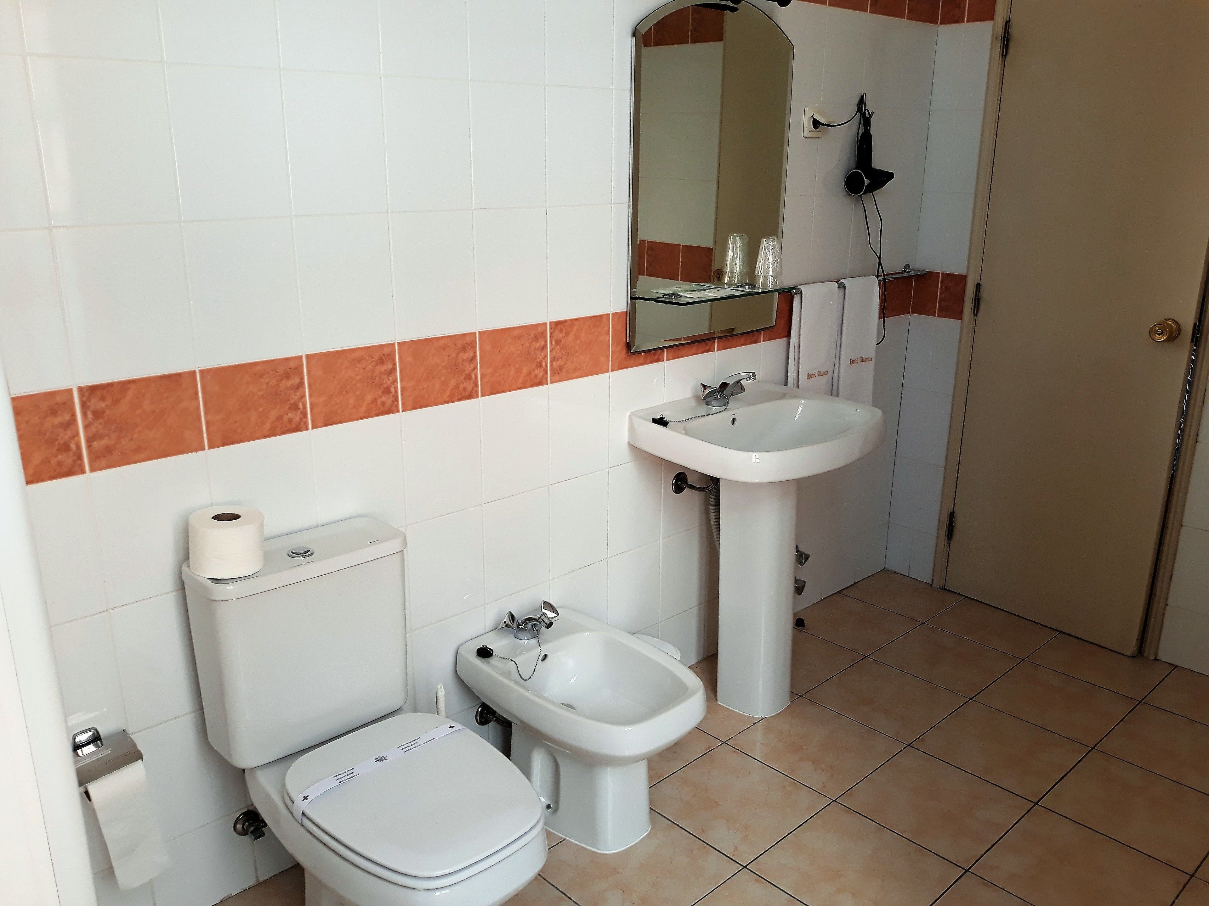 Et badeværelse med toilet, bidet, vask og et spejl.
