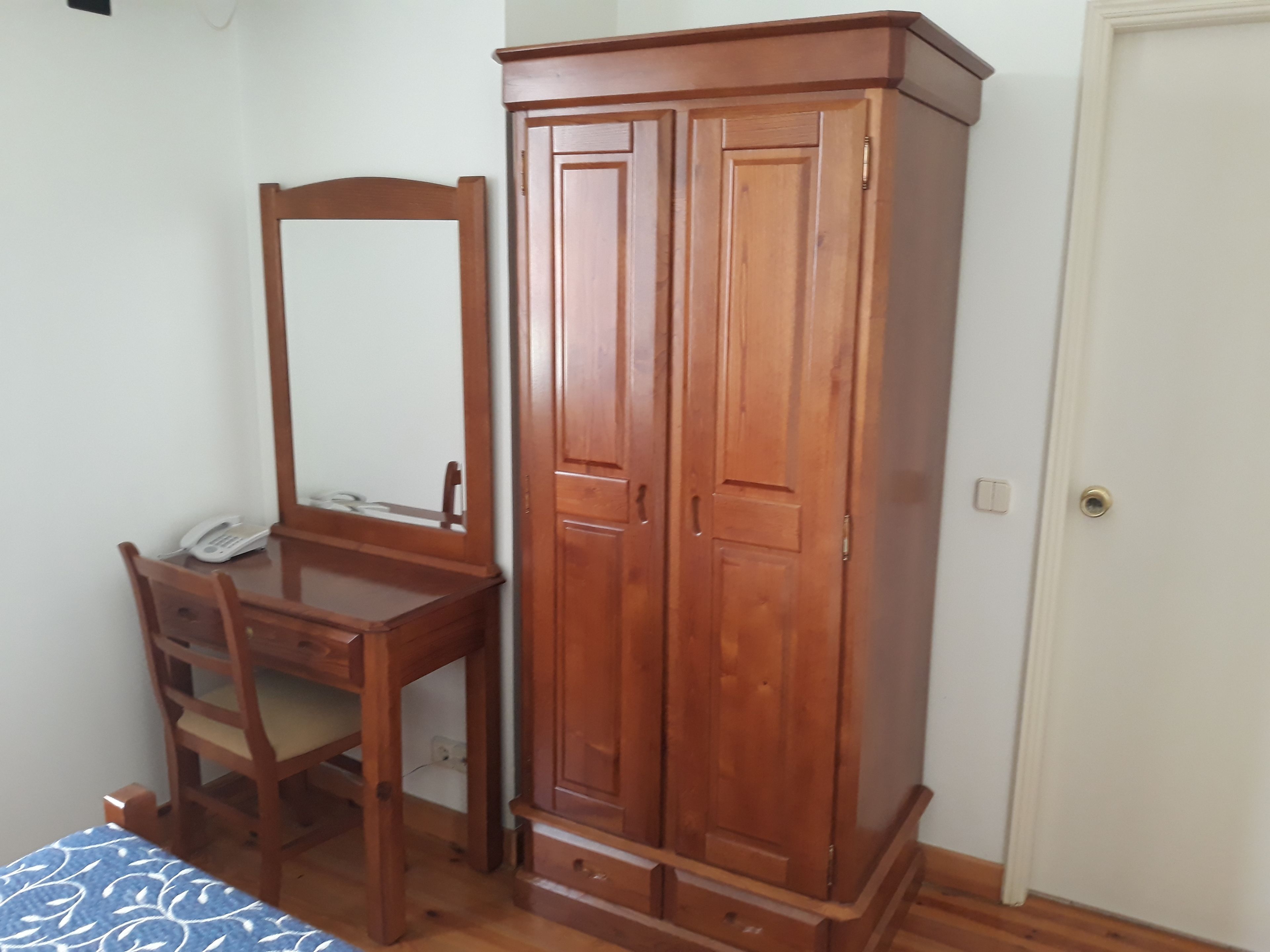 Un dormitorio con escritorio de madera, silla y armario.