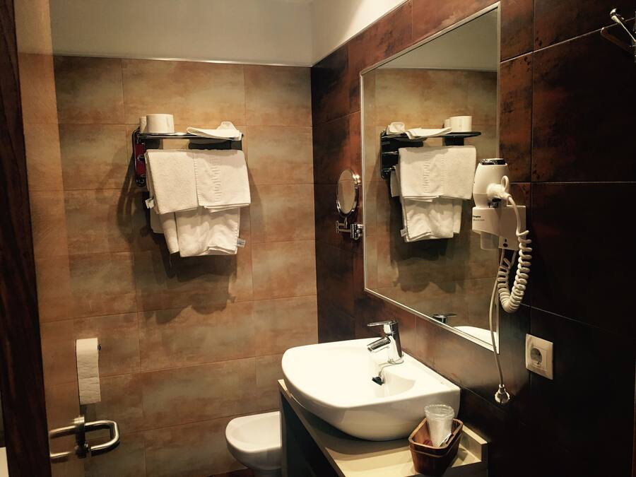 Une salle de bain moderne avec un lavabo, des toilettes et un miroir. Des serviettes sont accrochées à des crochets et un sèche-cheveux est fixé au mur.