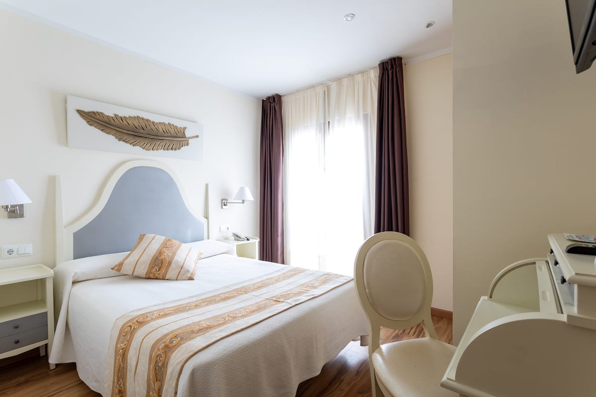 Una habitación de hotel con cama, mesitas de noche, escritorio y una silla.