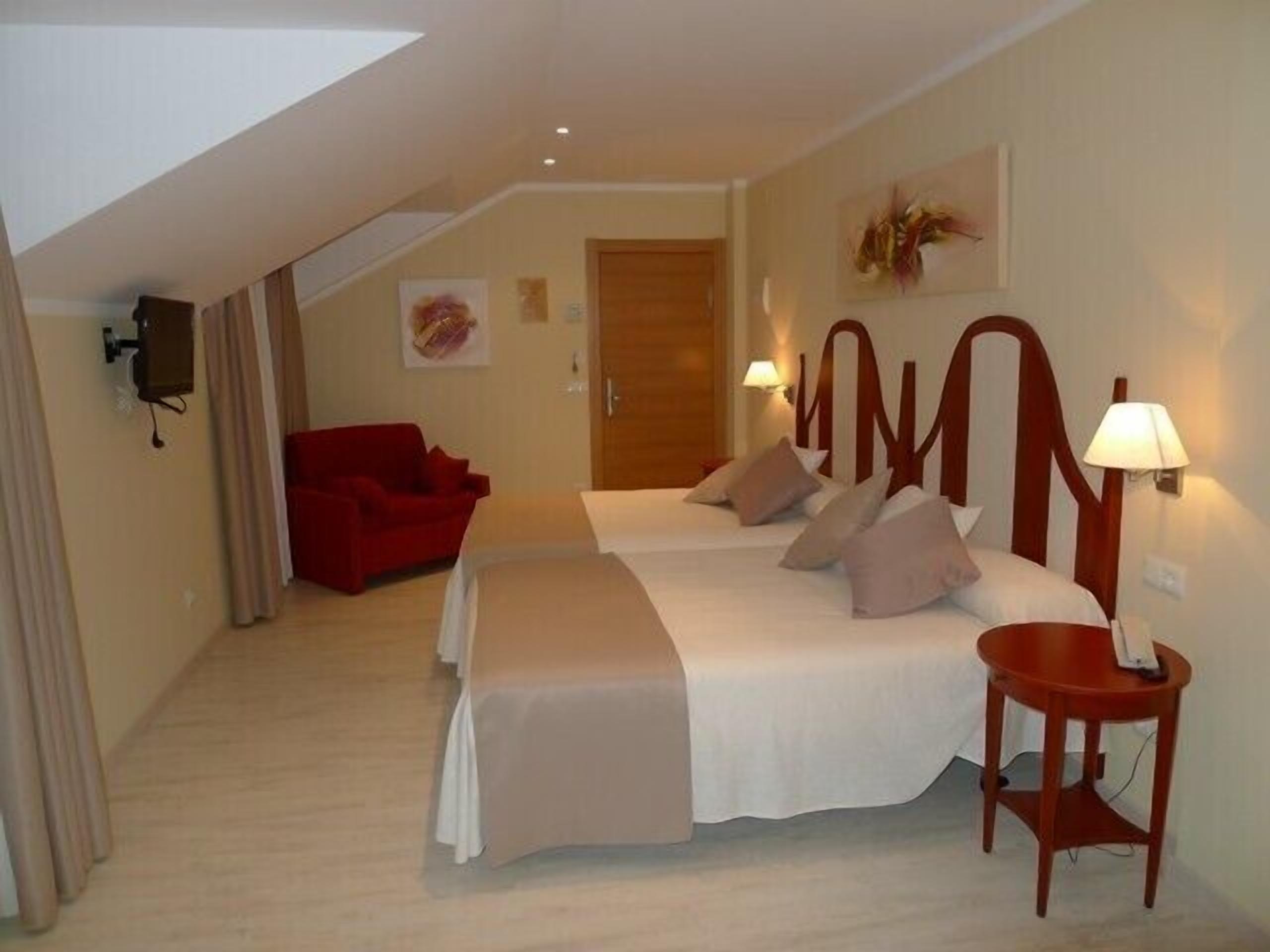 Una habitación de hotel con una cama grande, un sofá rojo y una pequeña mesa con lámpara.