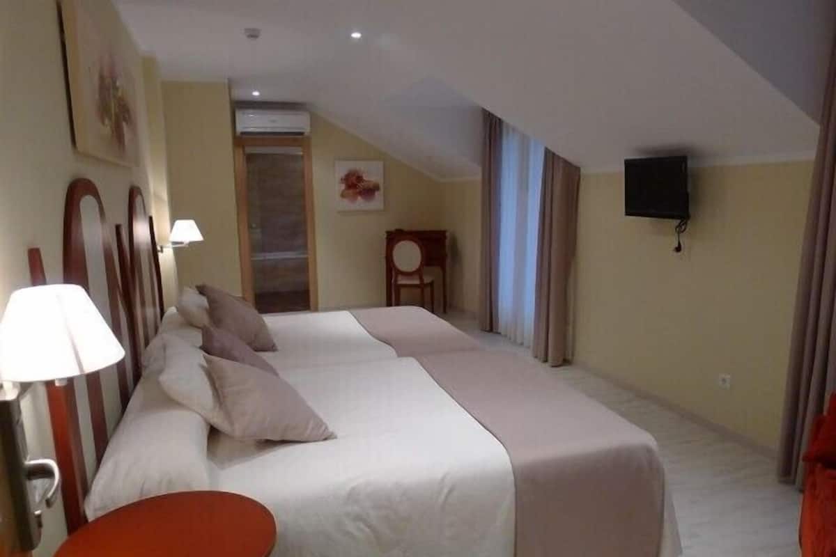 Habitación de hotel con una cama grande, una mesita pequeña, un televisor en la pared y una ventana con cortinas.