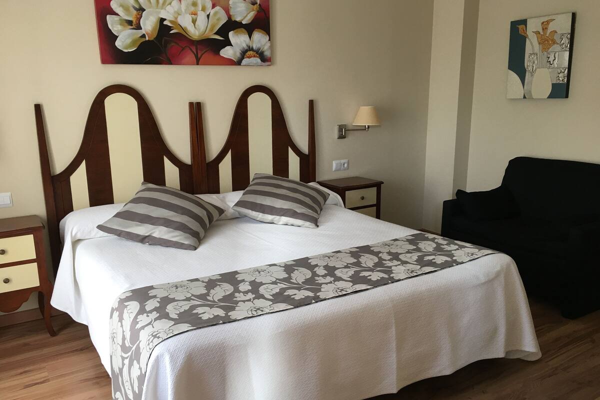 Una cama bien hecha con un edredón estampado con motivos florales, un cabecero de madera y dos mesitas de noche con lámparas.
