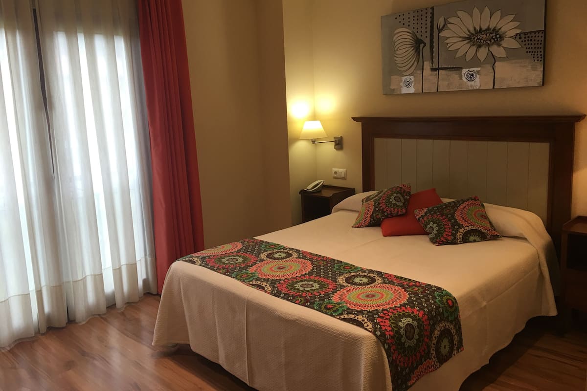 Una habitación de hotel con cama, mesita de noche, lámpara y un cuadro en la pared.