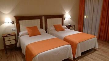 Quarto de hotel com duas camas, cada uma com colcha laranja e cabeceira branca. Há mesas de cabeceira com abajures e uma mesinha de cabeceira com telefone.