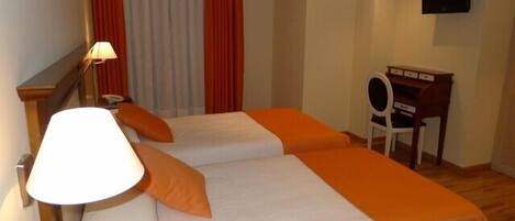 A hotel room with two beds, a desk, a chair, a lamp, and a TV.