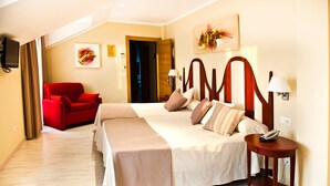 A hotel room with a large bed, a red armchair, a bedside table with a lamp, and artwork on the walls.