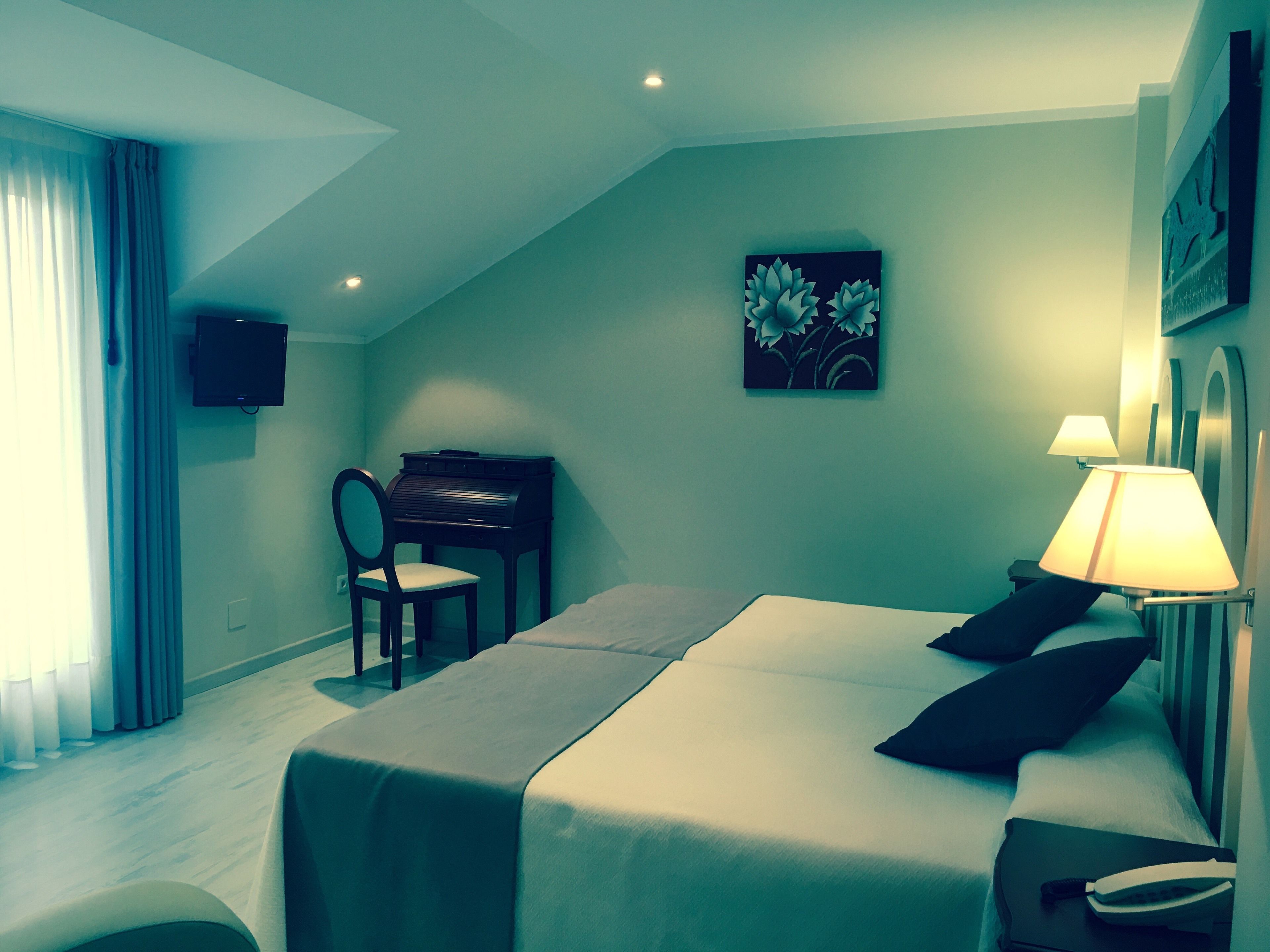 A hotel room with a bed, a desk with a chair, a television, and a painting on the wall.