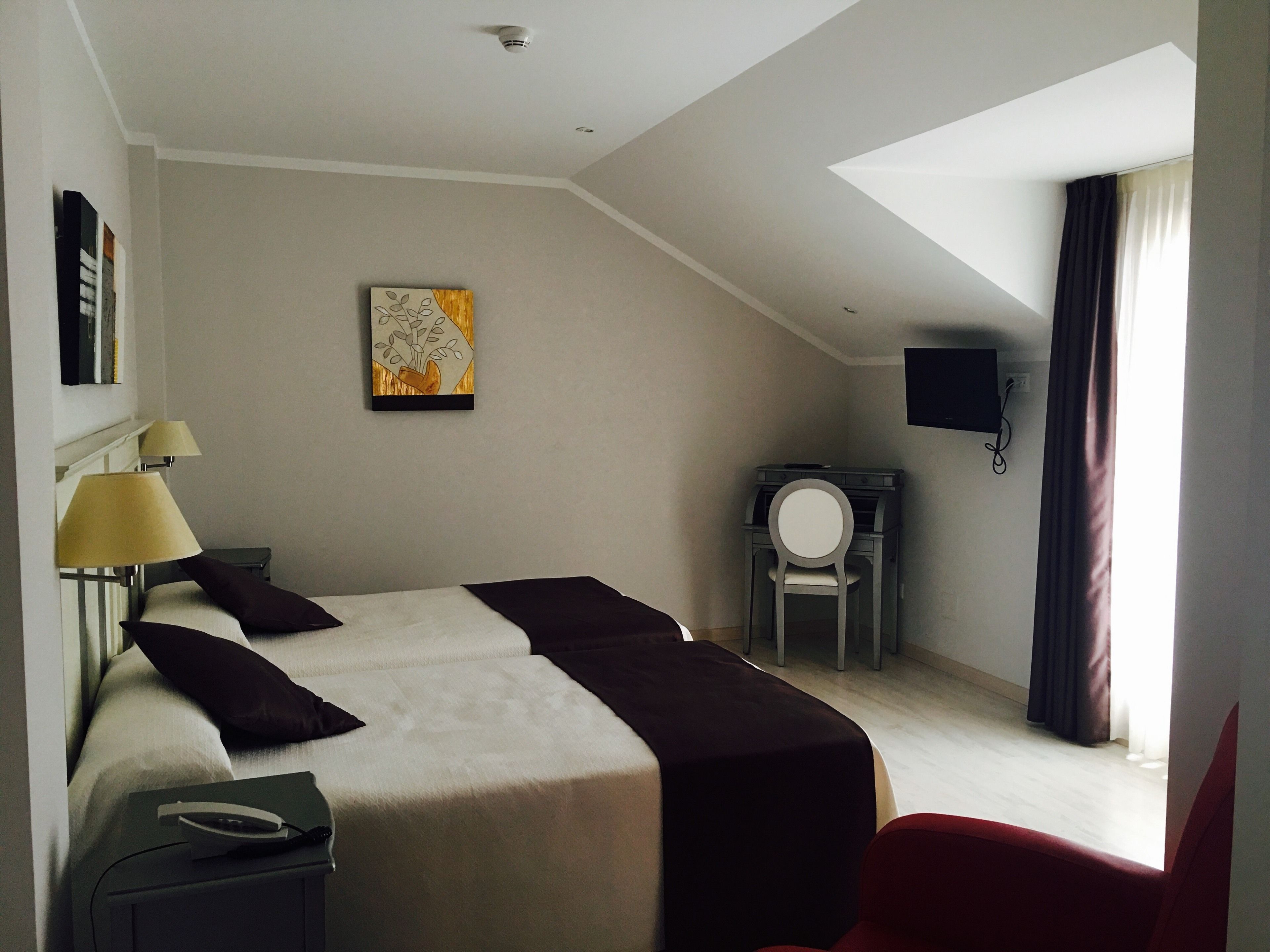 Habitación de hotel con cama, escritorio, silla, televisor y un cuadro en la pared.