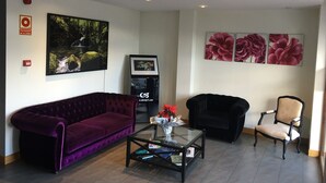 A living room with a purple sofa, a black armchair, a glass coffee table, and a wall-mounted TV.