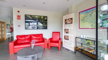 Zona de recepción con un sofá rojo, una mesita de centro, un mapa y una bandeja con pasteles.