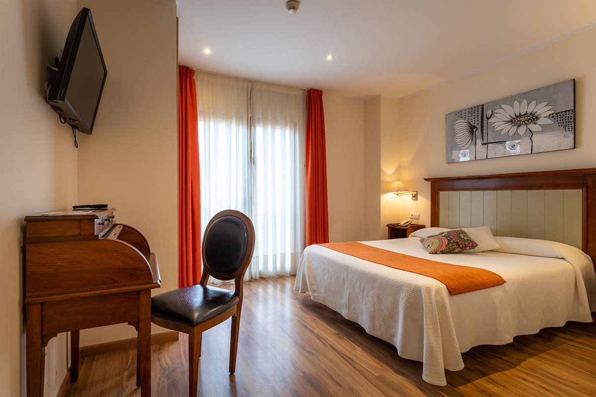 Habitación de hotel con cama, escritorio, silla, televisión y un cuadro en la pared.