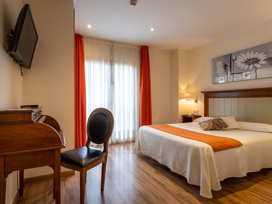 Una camera d'albergo con un letto, una scrivania, una sedia, una televisione e un quadro appeso al muro.