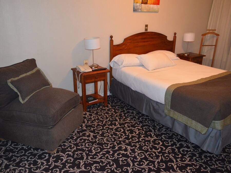 A hotel room with a bed, a chair, a nightstand, and a lamp.