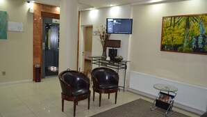A reception area with two leather chairs, a glass table, a TV, a painting, and an elevator. - Hotel Don Eduardo (Temuco)