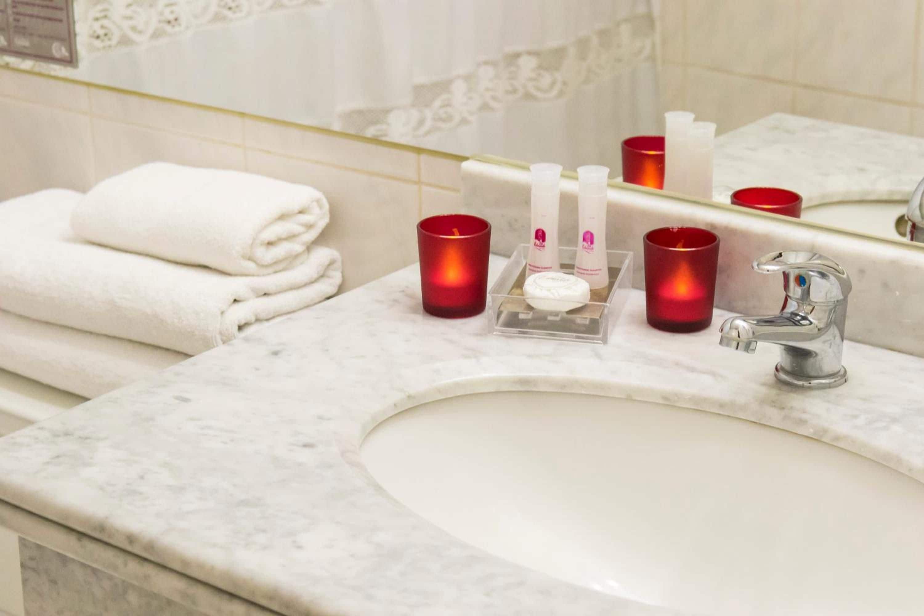 Ein Badezimmer mit Marmorwaschbecken, einem Spiegel und Pflegeprodukten, darunter Kerzen und einer Seifenspender.