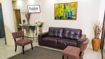 A reception area with a brown leather sofa, two matching armchairs, a patterned rug, a coffee station, and a painting of a forest scene.