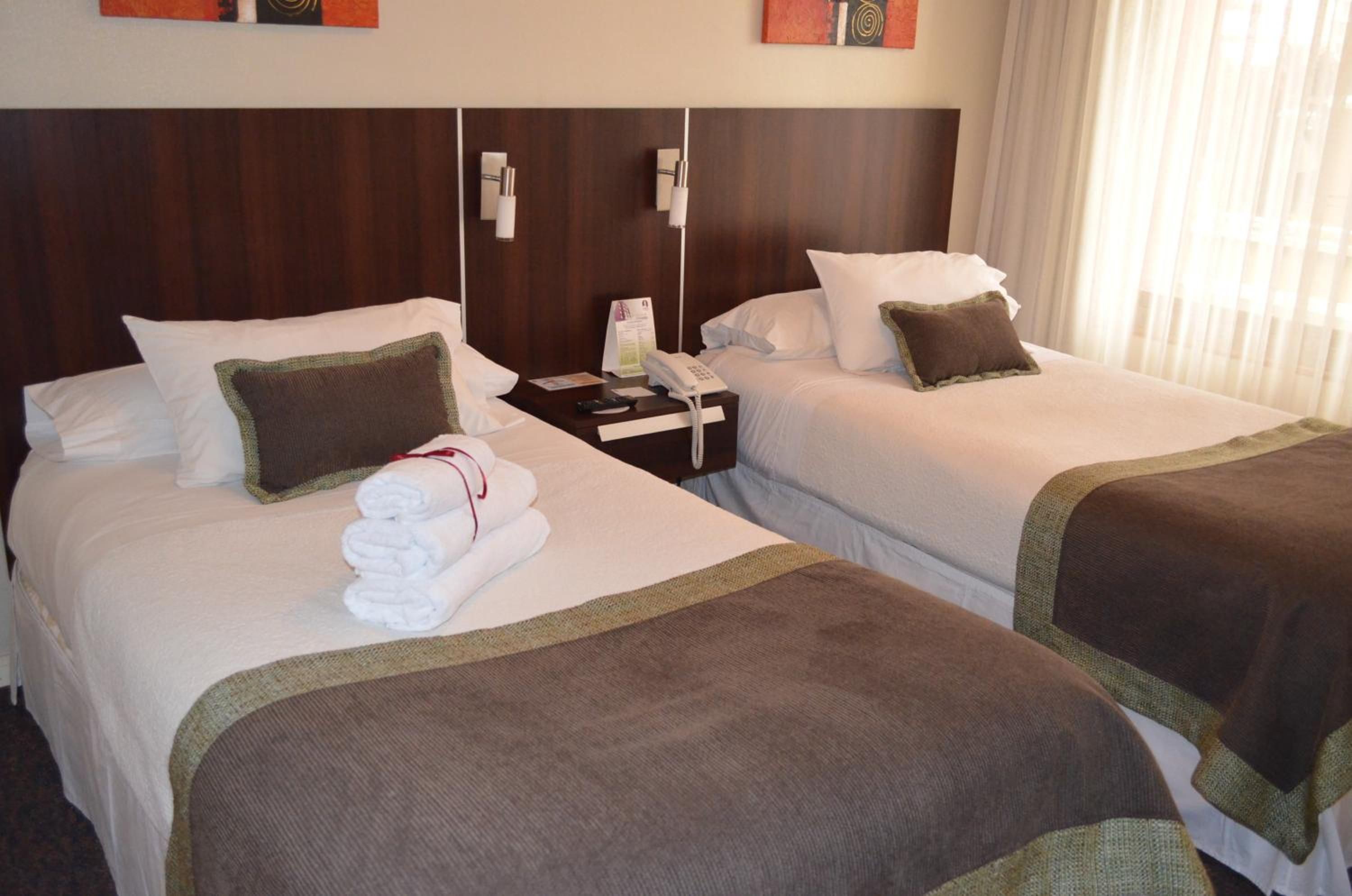 A hotel room with two beds, each with a pillow, a bedside table with a phone, and a folded towel.