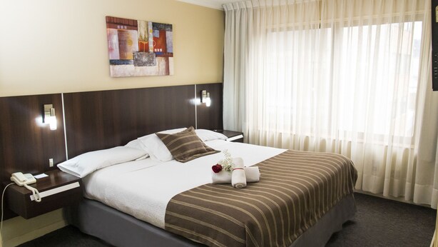 A hotel room with a large bed, a bedside table with a phone, a wall-mounted light, and a window with sheer curtains. - Hotel Don Eduardo (Temuco)