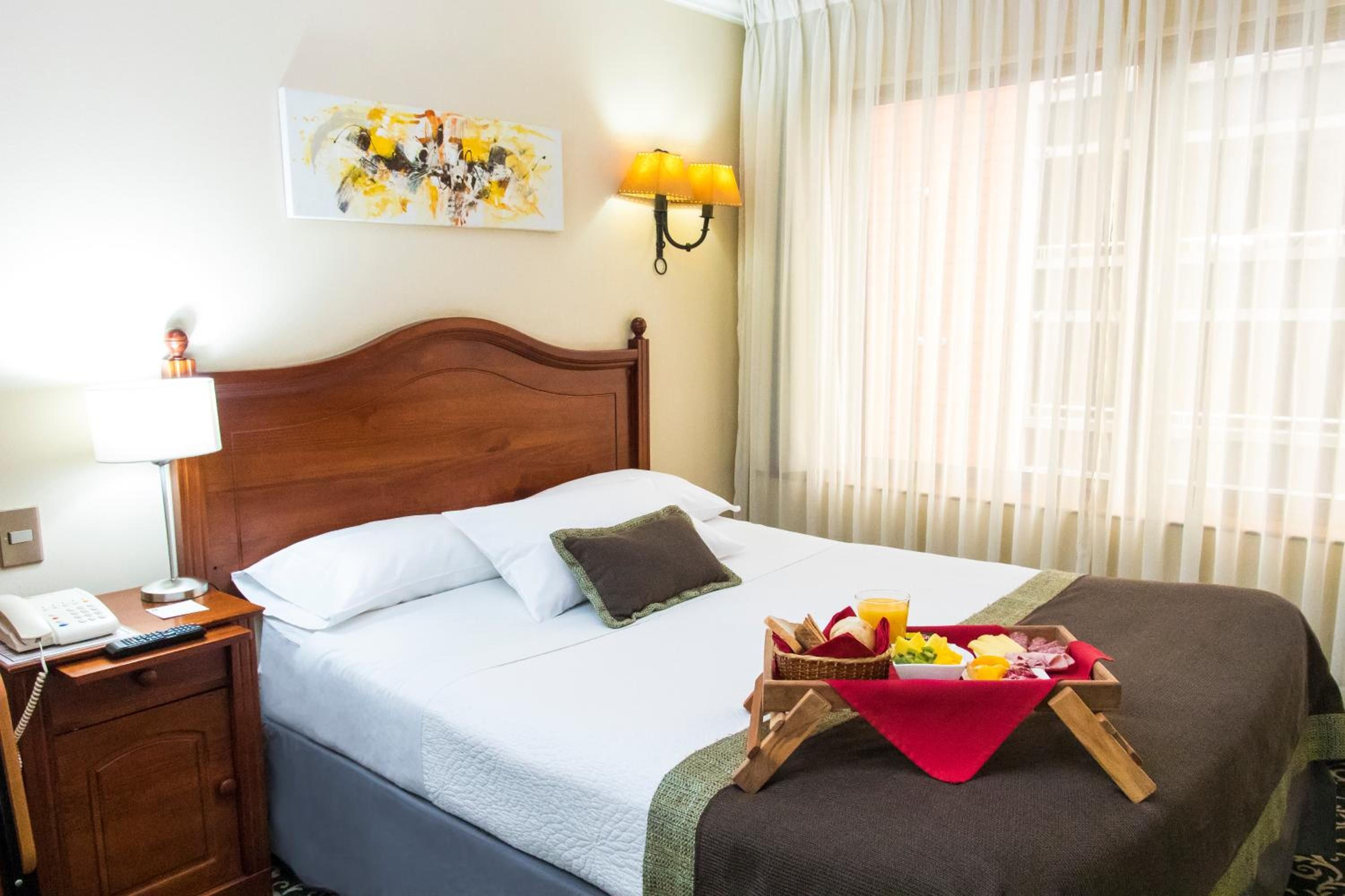 Una habitación de hotel con una cama bien hecha, una mesita de noche con una lámpara, un teléfono y una obra de arte colgada en la pared.