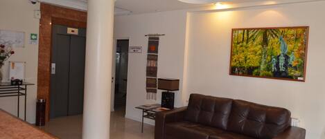 A lobby with a brown leather sofa, a coffee station, a painting, and a sign pointing to the cafeteria.