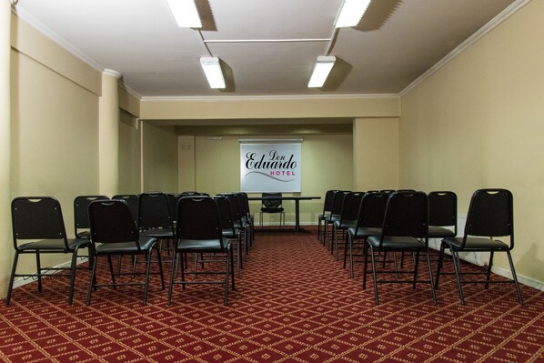 Un salón de conferencias con filas de sillas negras mirando hacia una pizarra donde está escrito 'Eduardo Hotel'.