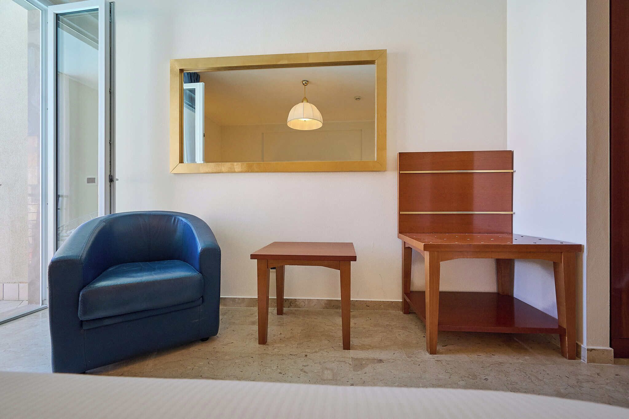 Ein Zimmer mit einer Schiebetür aus Glas, einem blauen Ledersessel, einem kleinen Holztisch und einem Holzschrank.