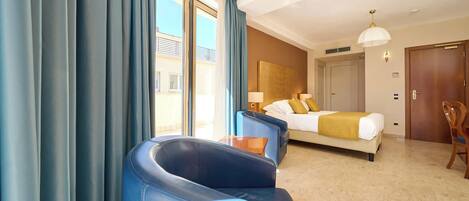 A hotel room with a bed, two blue chairs, a table, a lamp, and a view of the outside.