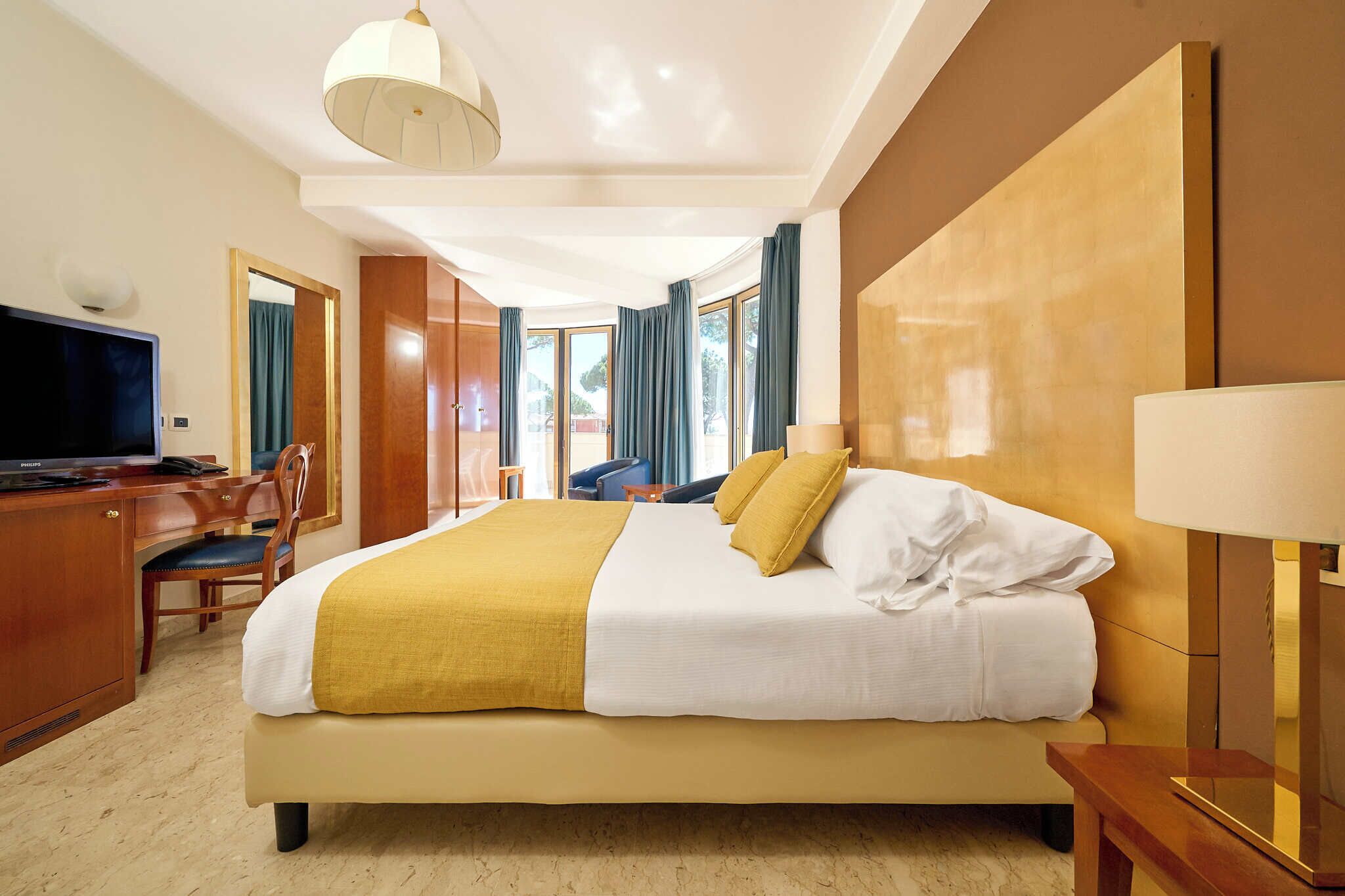 Habitación de hotel con una cama grande, un escritorio con televisor y vistas al exterior a través de amplias ventanas.