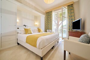 Habitación de hotel con cama, televisión, una silla y balcón con cortinas.