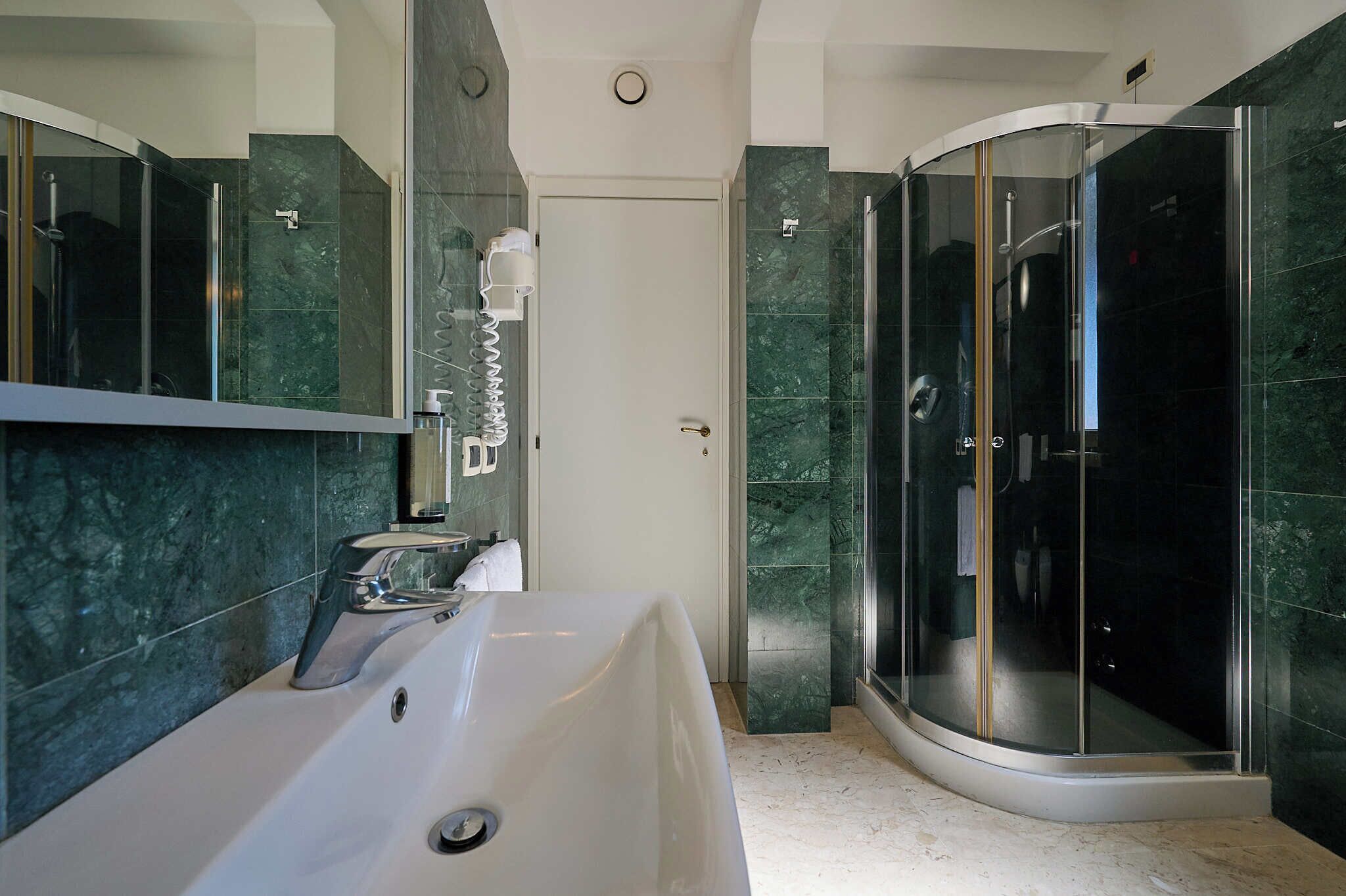 Un baño moderno con un espejo grande, un lavamanos, cabina de ducha y una puerta.