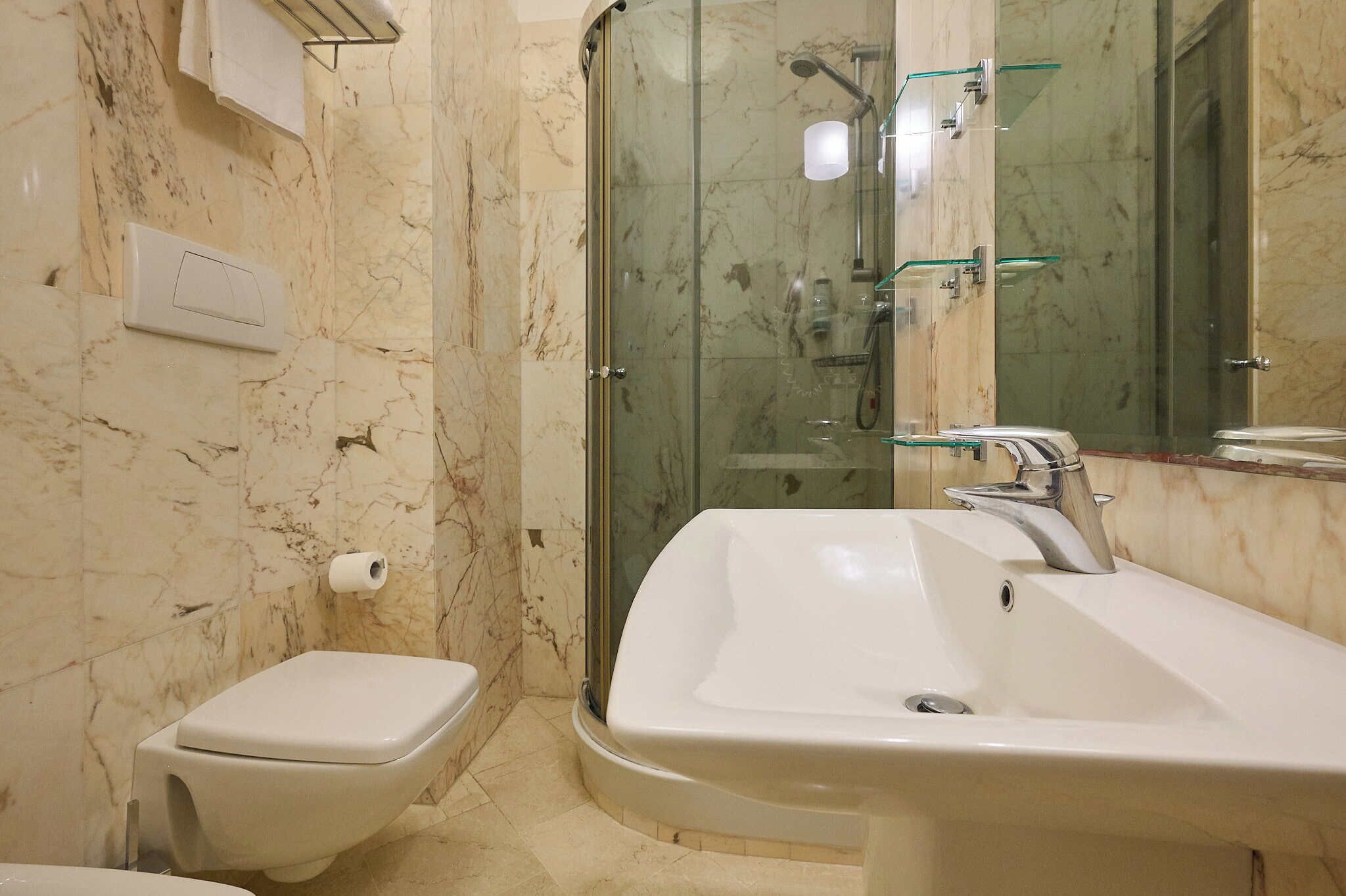 Une salle de bain comprenant des toilettes, un lavabo, un espace douche et un mur recouvert de carreaux de marbre.