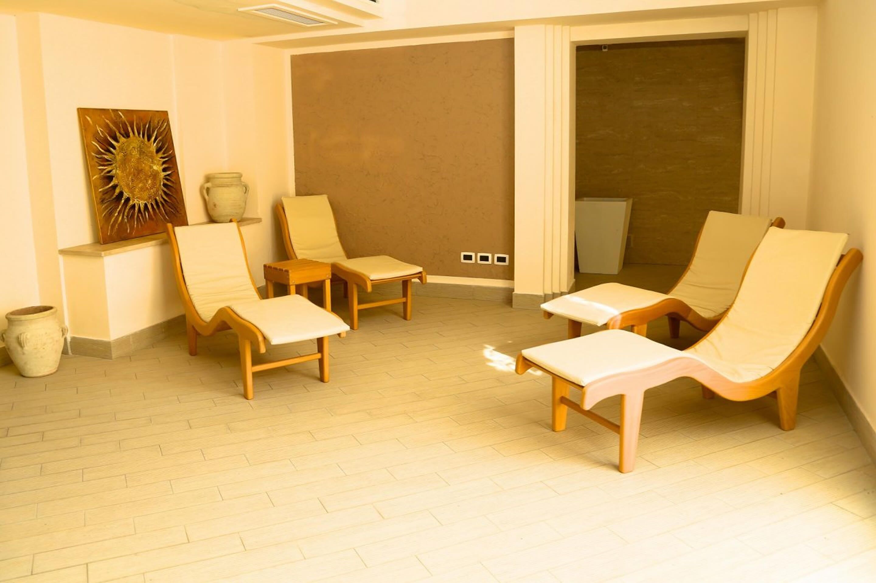 A room with four wooden lounge chairs, a small table, and a decorative sunburst painting on the wall.