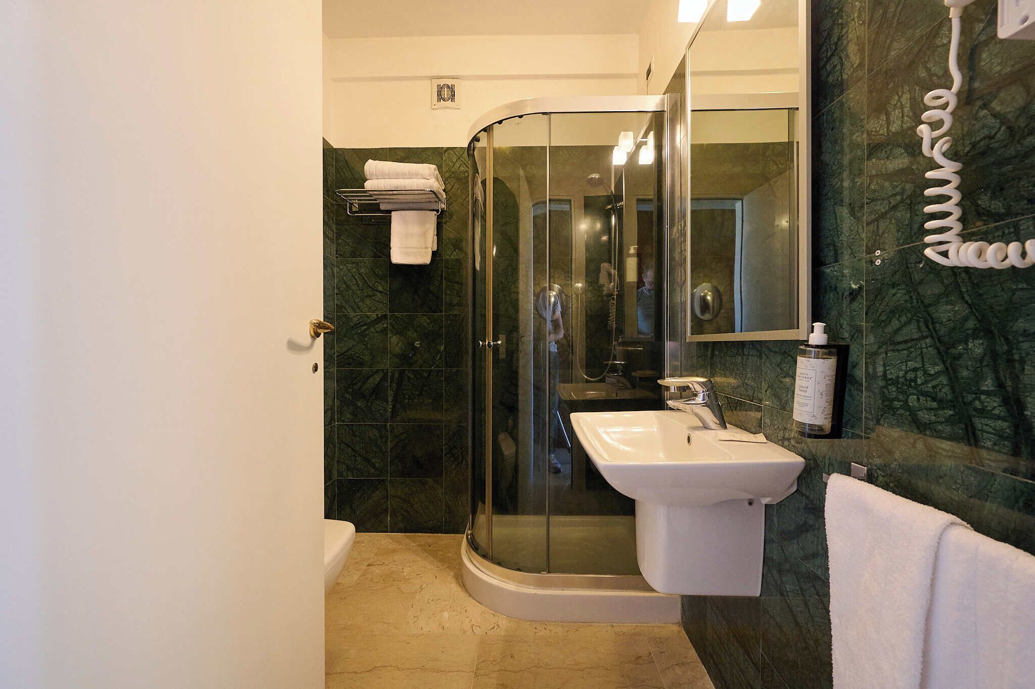 Ein modernes Badezimmer mit einer gläsernen Duschkabine, einem weißen Waschbecken und einer marmorverkleideten Wand.