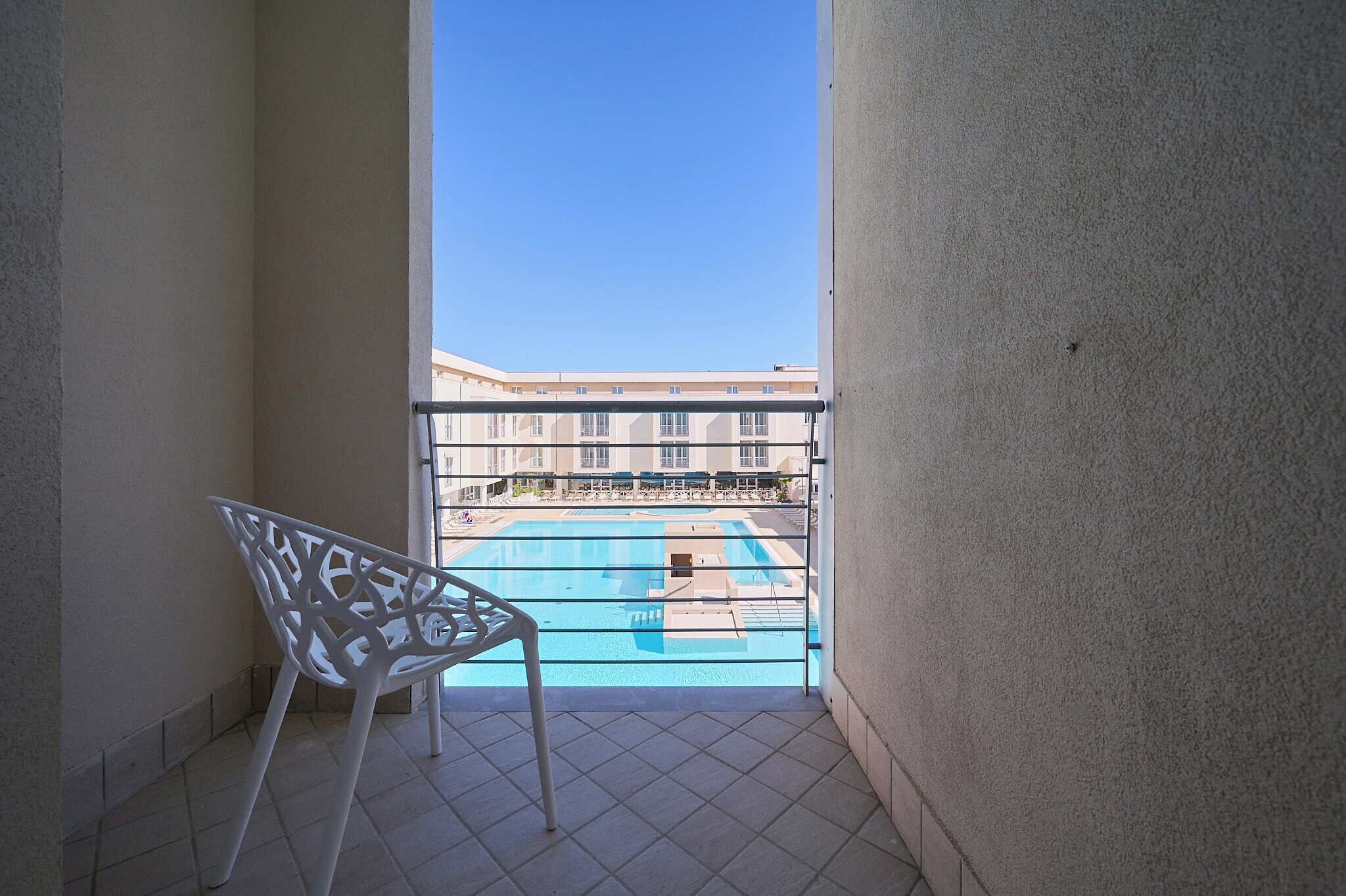 A balcony with a view of a swimming pool and a building in the background.