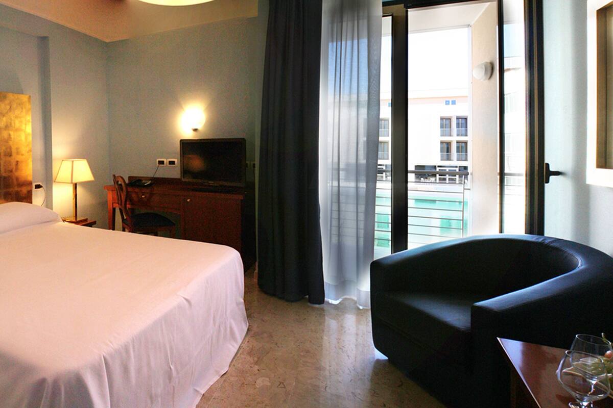 Ein Hotelzimmer mit Bett, Schreibtisch mit Fernseher, Stuhl und Balkon mit Aussicht.