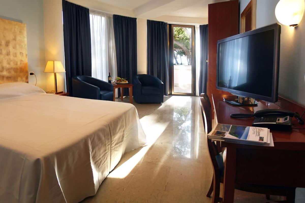 Ein Hotelzimmer mit einem Bett, einem Schreibtisch mit Computer, einem Fernseher und einem Sessel.