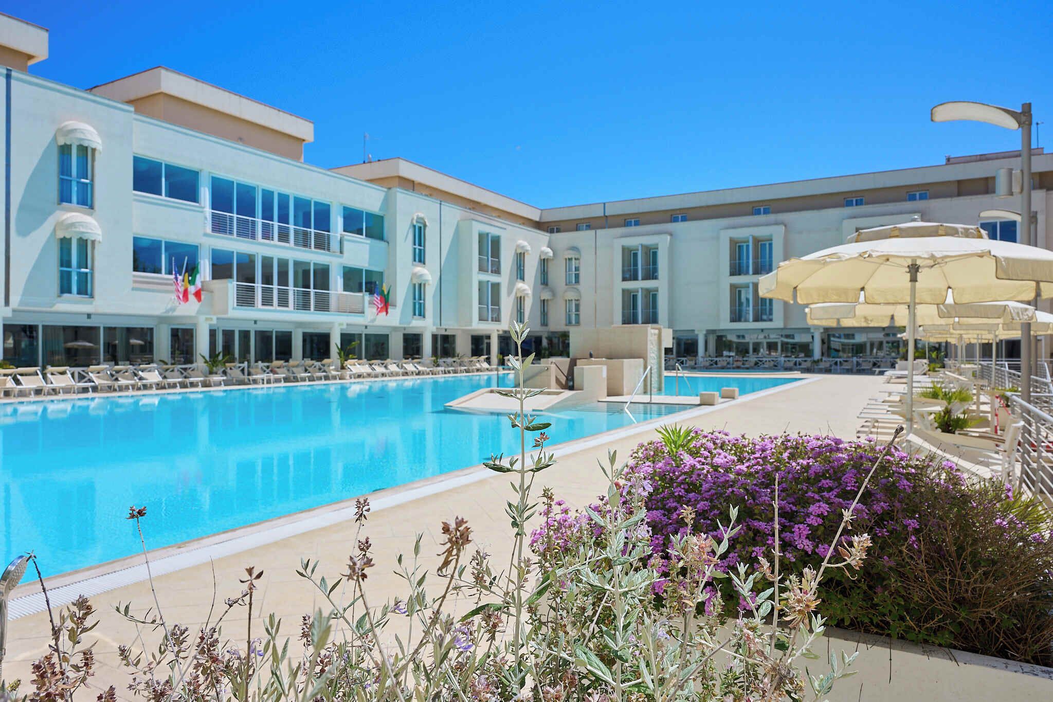 A hotel with a swimming pool, lounge chairs, and umbrellas.