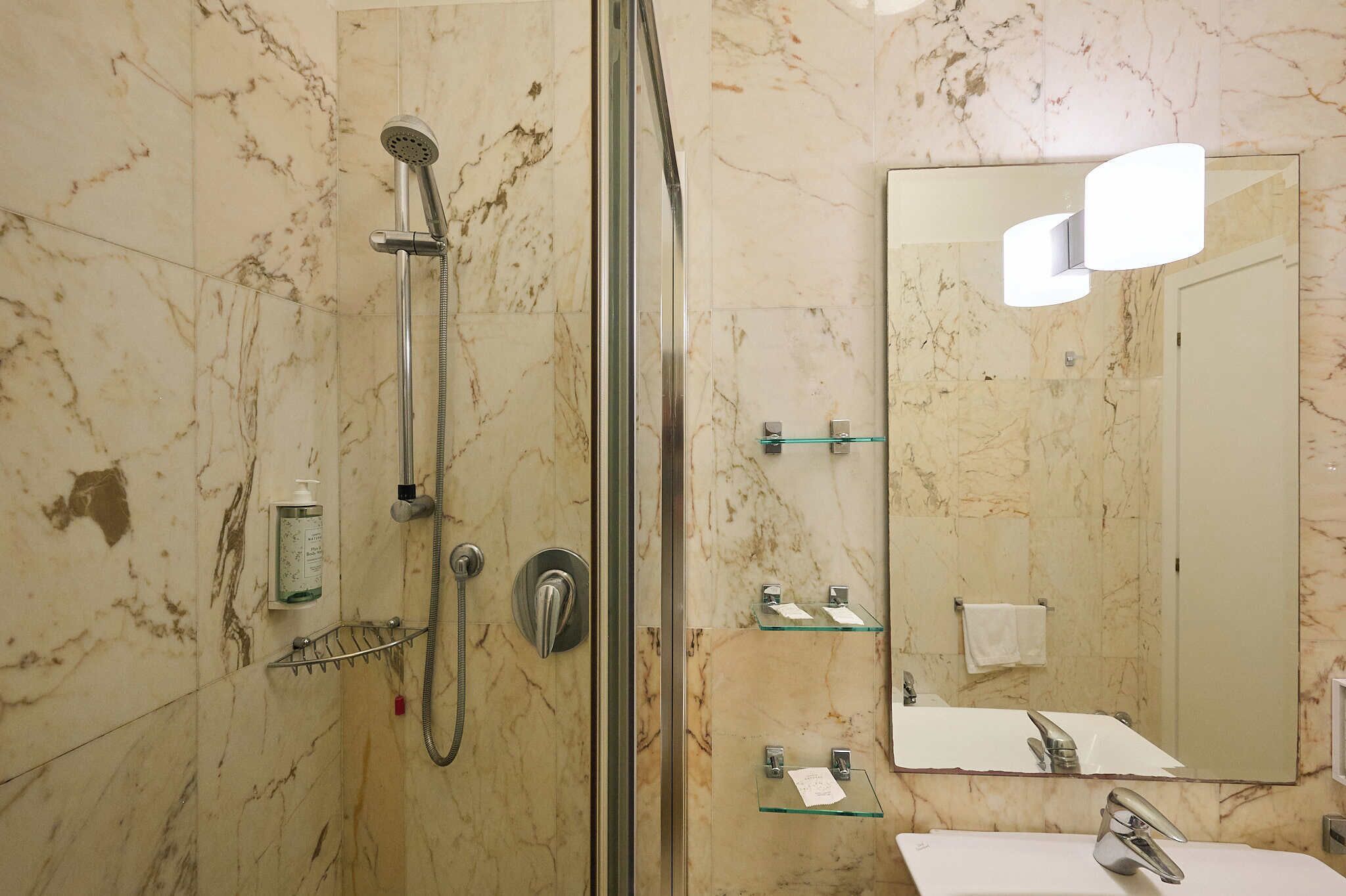 A bathroom with a shower, a sink, a mirror, and marble walls.