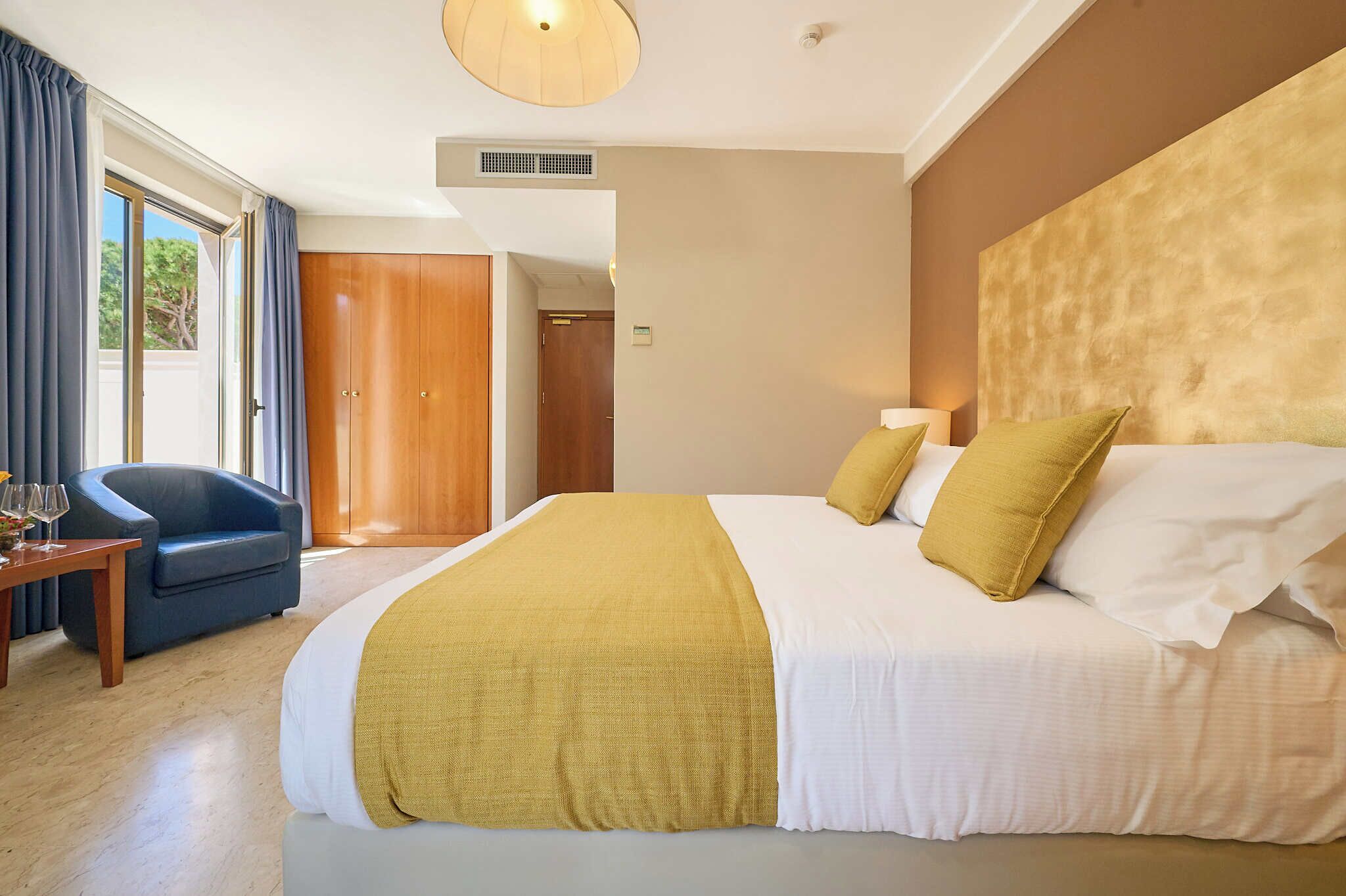 A hotel room with a large bed, a desk, a chair, and a view of the outdoors.