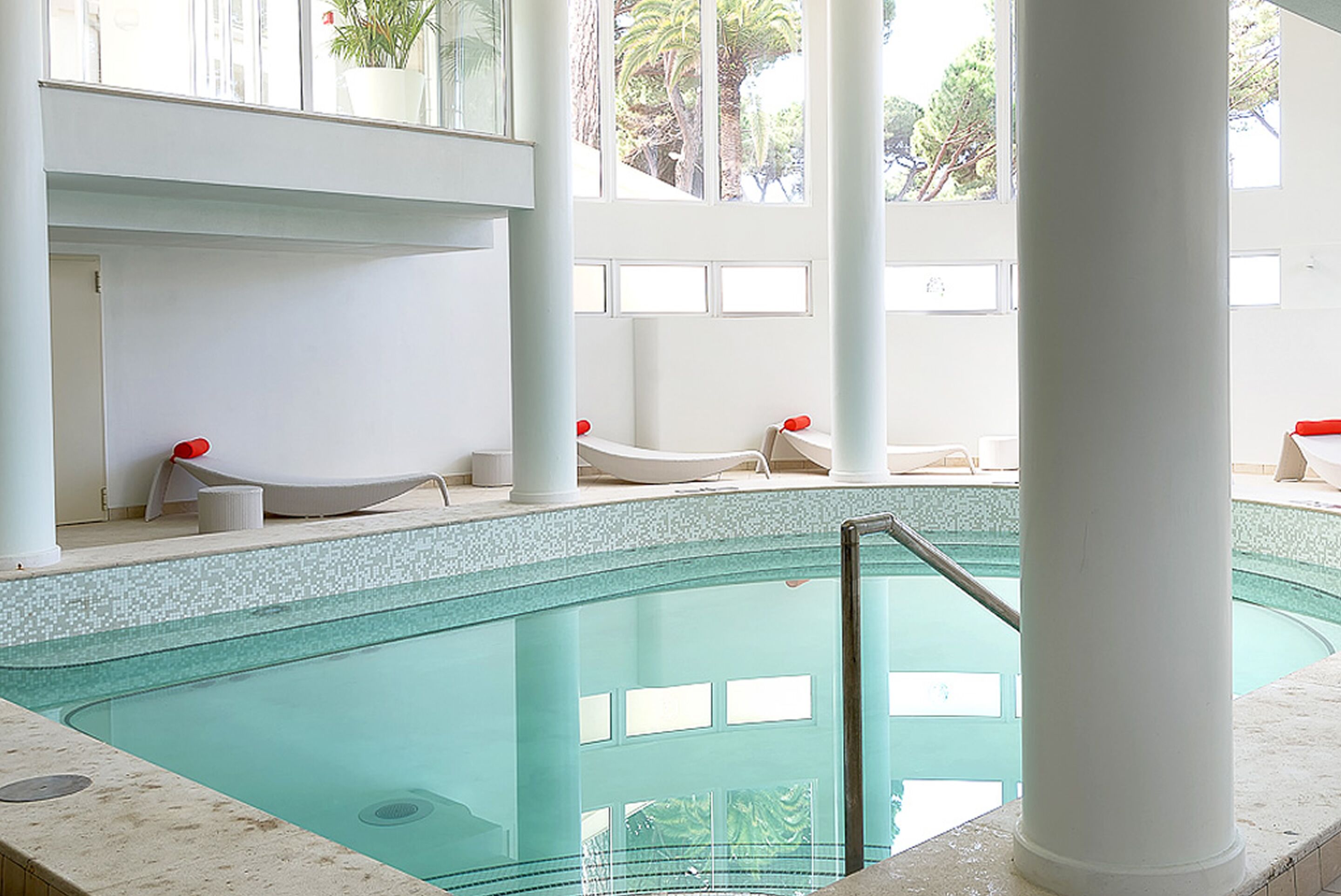 Une piscine à l’eau claire, entourée de colonnes blanches et dotée d’une terrasse carrelée.