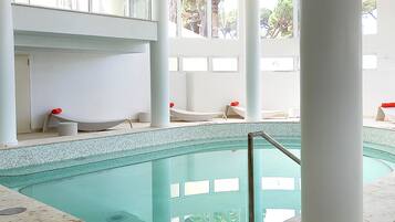 Une piscine à l’eau claire, entourée de colonnes blanches et dotée d’une terrasse carrelée.