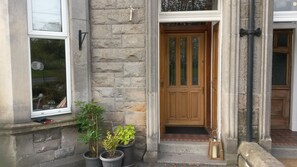 A stone building with a wooden door, potted plants, and a window. - Ravenswood Guest House (Stirling)