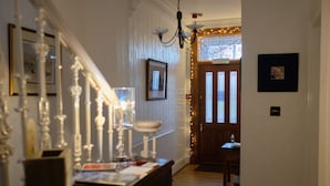 A hallway with a wooden bench, a chandelier, and a door with a window. - Ravenswood Guest House (Stirling)