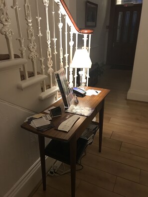 A wooden desk with papers, a lamp, and a laptop in a hallway with a white railing and wooden floor. - Ravenswood Guest House (Stirling)