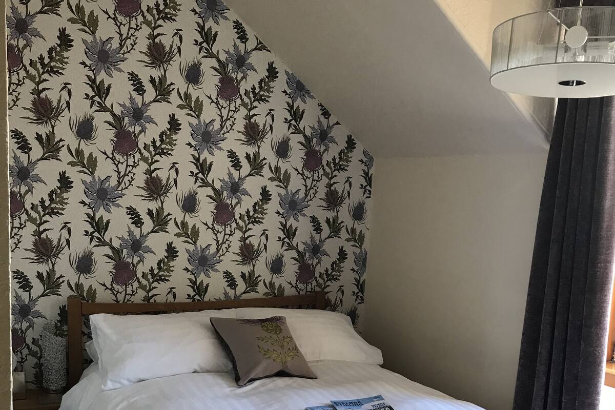 Un lit bien fait, avec du linge de lit blanc et une tête de lit à motifs floraux.