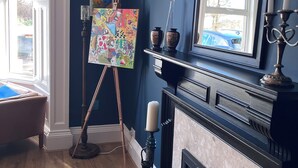 A room with a fireplace, a large mirror, and a painting on easels. - Ravenswood Guest House (Stirling)